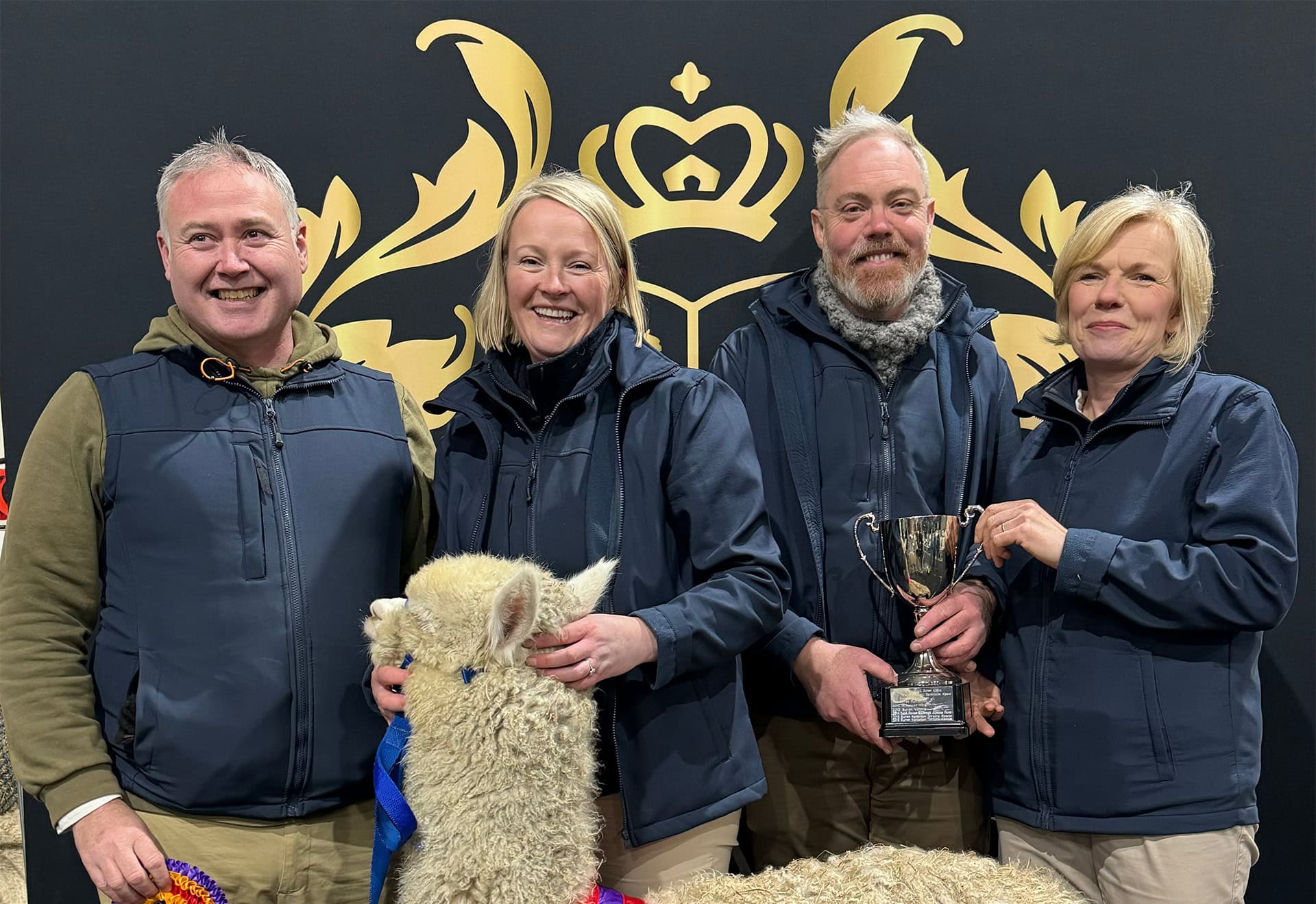Four people with a llama holding a trophy, smiling.